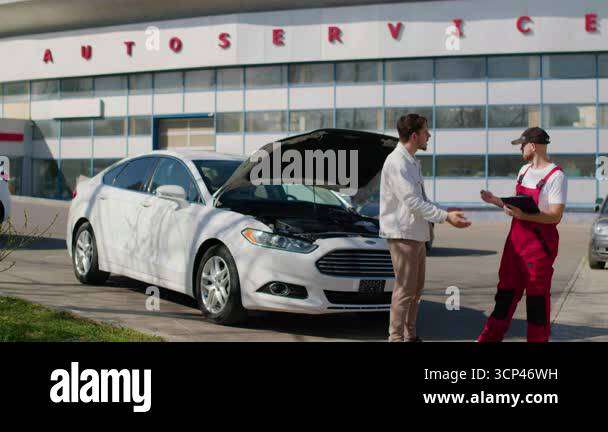 Automotive technician in red overalls engages with customer about car ...
