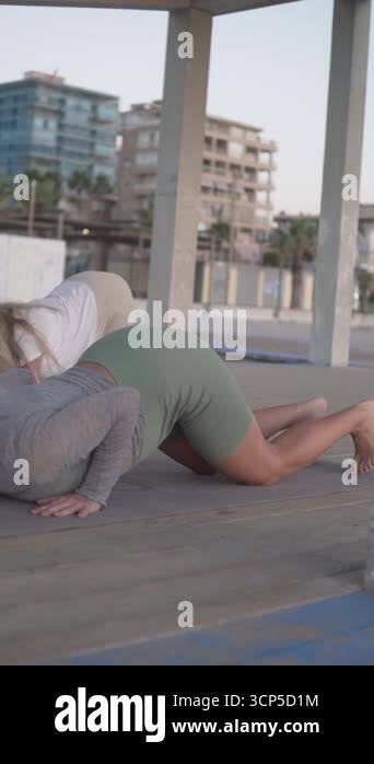 A pregnant woman is practicing yoga on a wooden deck at the beach. She ...