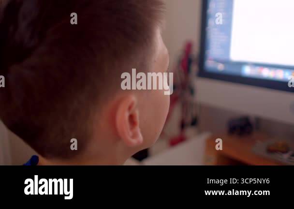 A young boy sits at a computer, absorbed by the screen. His expression ...