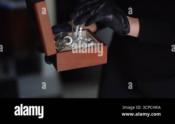 A girl burglar in black gloves carefully takes valuable jewelry from a ...