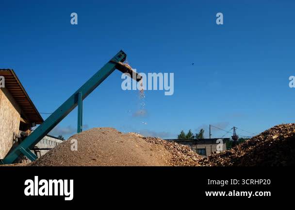Wooden sawdust splinters pour out of chopping machine pipe against sky ...