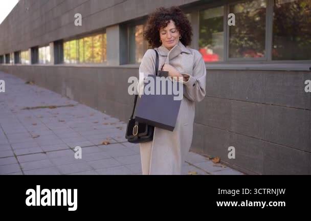 A confident woman dressed stylishly in a chic trench coat is carrying a ...