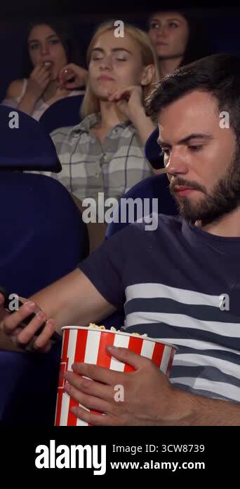 A young man with a striped popcorn bucket is distractedly chatting on ...