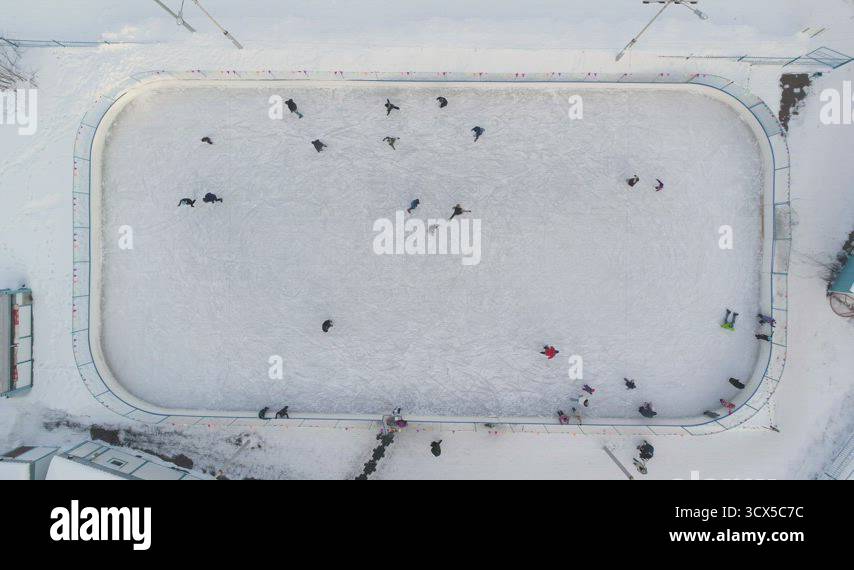 People are skating on ice rink in the sunny day. Aerial vertical top ...