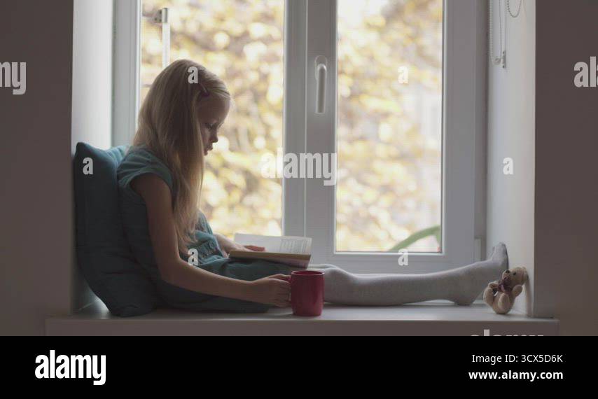 Child girl in turquoise dress reading book and drinks from red cup ...