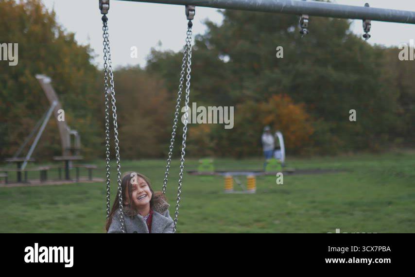 Joyful little girl on a swing pushed by her mother in a park Stock ...