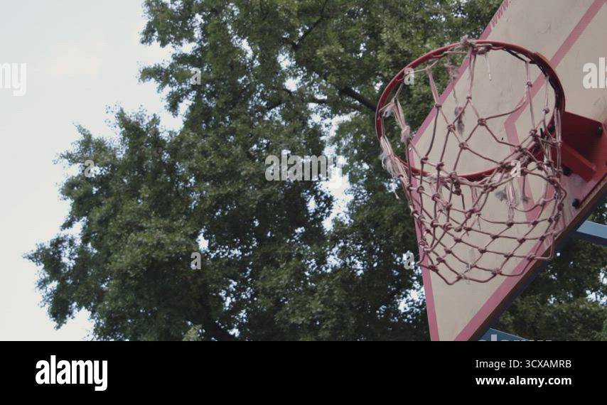 Thrown orange basketball cleanly hits the basket on an outdoor court in ...
