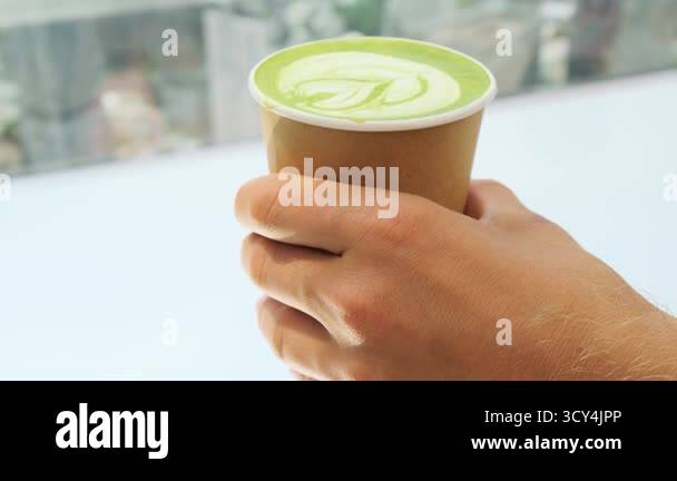 Hand holding paper cup of green tea matcha latte with white foam art ...