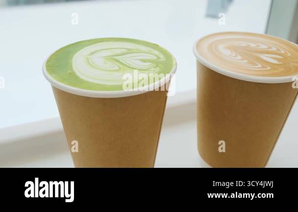 Two takeaway paper cups with matcha latte and cappuccino topped with ...
