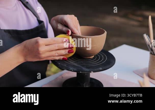 View of Potter smooths a clay bowl with a sponge on a wheel, refining shape and ...
