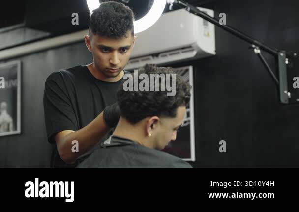 Young professional barber using an electric razor for a haircut on a ...