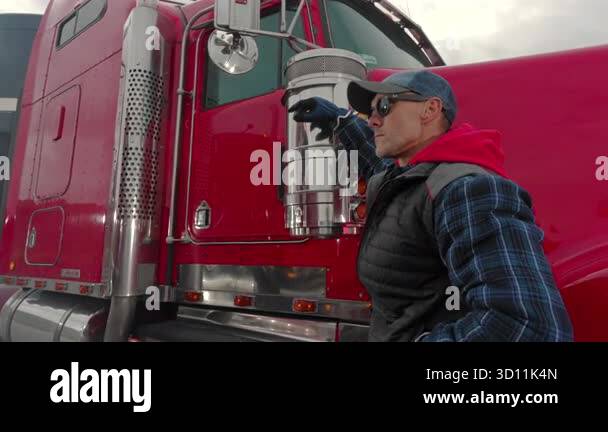 A driver checks the exhaust on their red truck at a rest stop while ...