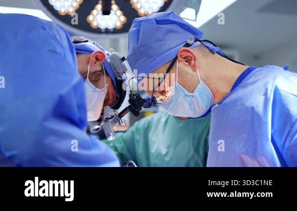 Focused faces of two male surgeons looking at operation through the ...