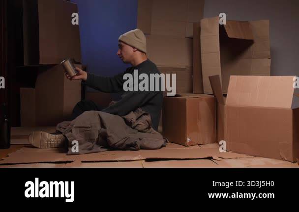 Homeless man sitting on cardboard boxes, holding a metal tin for ...