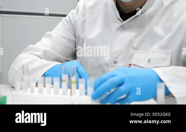Scientist in protective mask and cap placing blood test tubes in rack ...