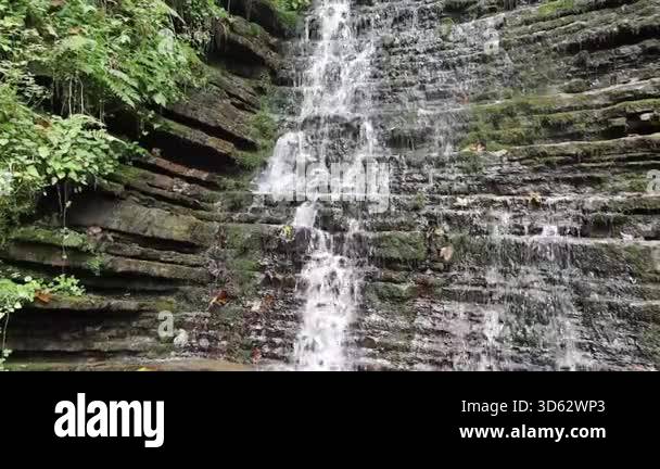 A powerful waterfall rushes over mossy rocks, splashing water and ...