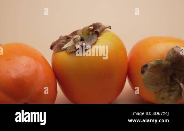 Three ripe persimmons rotate tightly grouped in a close-up shot. The ...