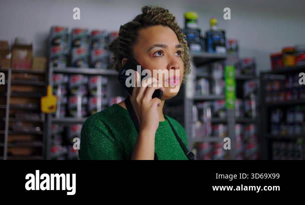 Focused shopkeeper on a phone call in a hardware store, shelves of ...