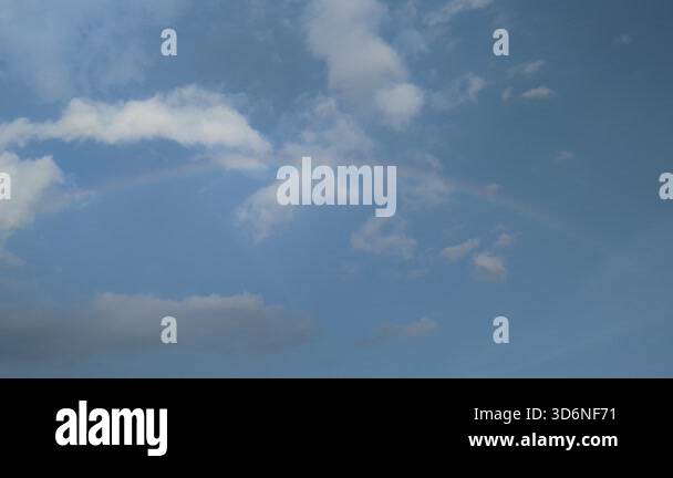 Rainbow stretches faintly across a clear blue sky with scattered fluffy ...