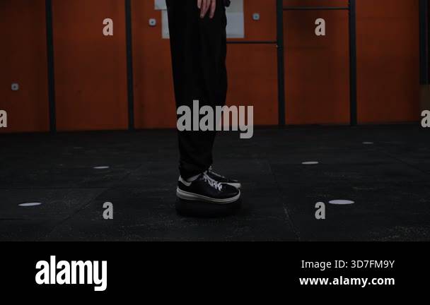 A man in a black suit stands on a balance sphere in the gym doing squat ...