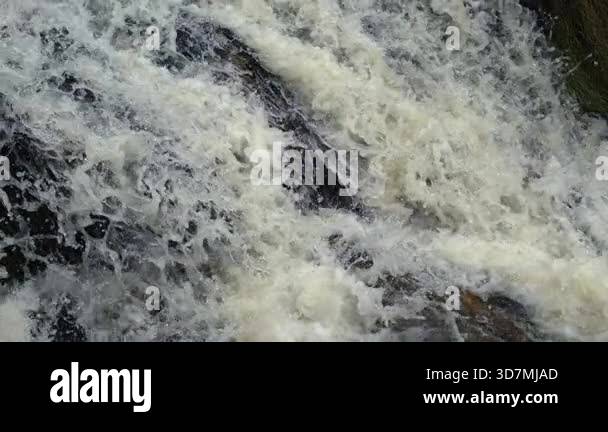 Detailed view of fast-flowing white water rushing over jagged dark ...