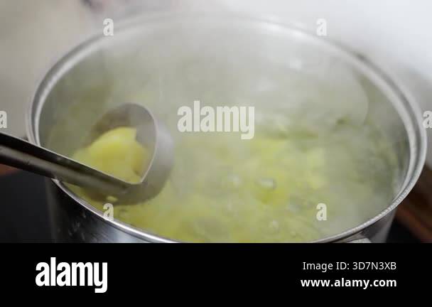 boiling potato cubes in stainless pot, steamy close-up of ladle lifting ...