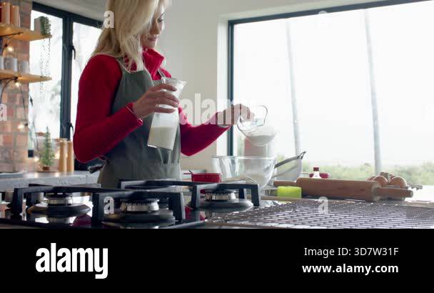 Woman starting baking at counter, pouring sugar into bowl, sliding milk ...