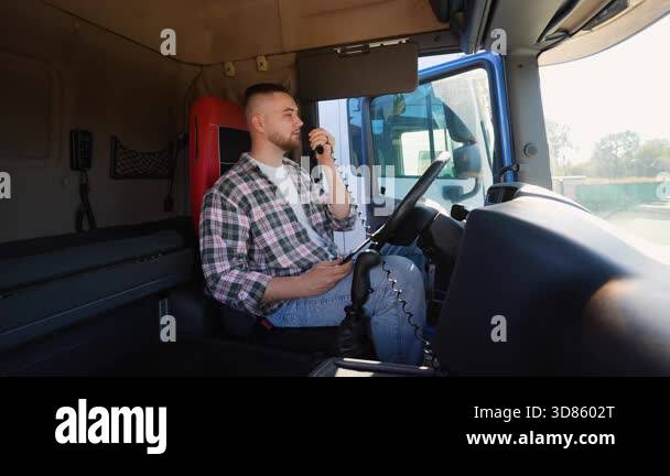 Young male trucker in a plaid shirt sitting inside a semi truck cabin ...