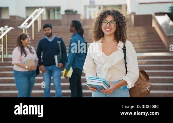 Young female university student with curly hair and glasses smiles ...