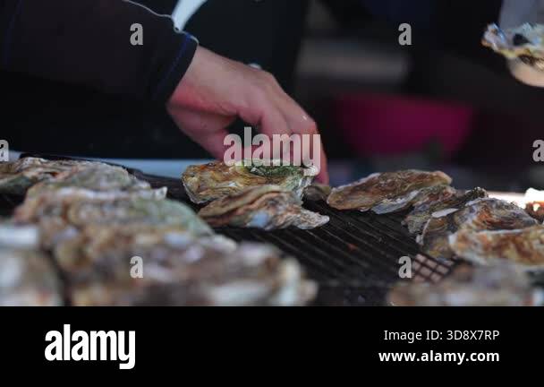 Close up shows a gloved vendor shucking and grilling oysters in ...