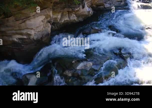 Rough white water cascades over dark rocks on a cliff side with green ...