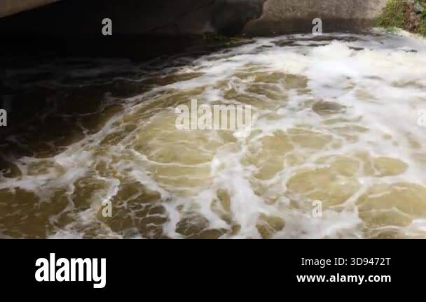 Rushing water flowing through concrete canal structure with foamy ...