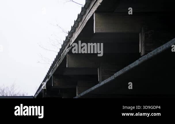 A low angle view of a dark wooden roof overhang with rain falling ...