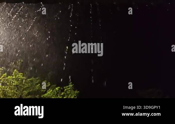 A cinematic video showing heavy rain falling at night, illuminated by a ...