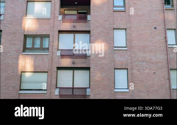 A brick mid-rise apartment facade featuring multiple windows and small ...