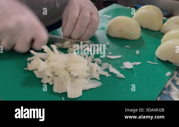 A chef wearing protective gloves quickly chopping peeled onions on a ...