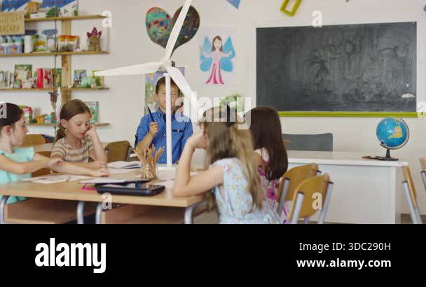 Curious schoolboy presenting wind turbine model to classmates in ...