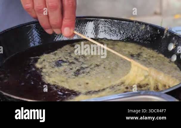 Cooking street food in hot oil inside a large frying pan; close up of ...