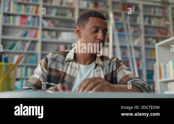 Focused African American man male student in library putting on glasses ...