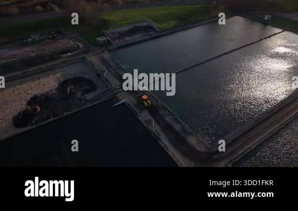 From above, an excavator digs at a fish farm. The ponds are rectangular ...