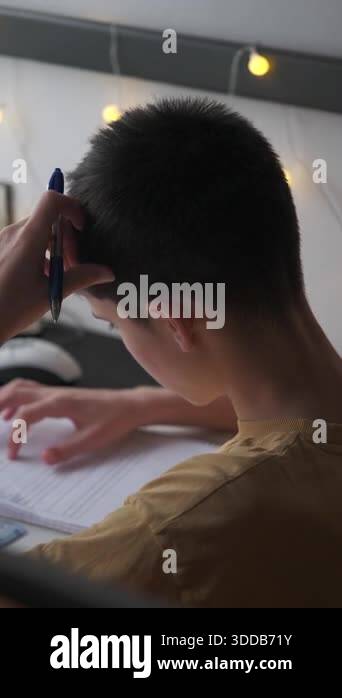 Vertical video of a pensive teenage boy holding a pen to his head while ...