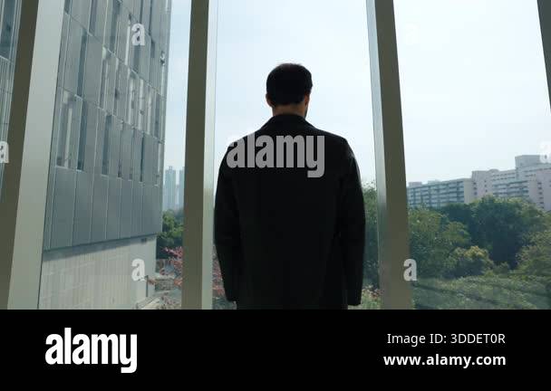 Businessman in black suit stands near panoramic window in office lobby ...