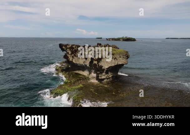Rock formation rises above the ocean with sharp edges and vegetation on ...