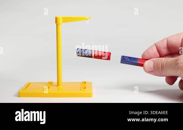 Hands manipulate magnets on a stand, illustrating magnetic attraction ...