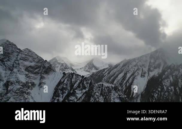 Majestic snow-covered mountains rise under a dramatic sky filled with ...