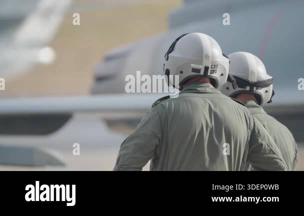 Two military pilots in flight suits and helmets standing near a fighter ...
