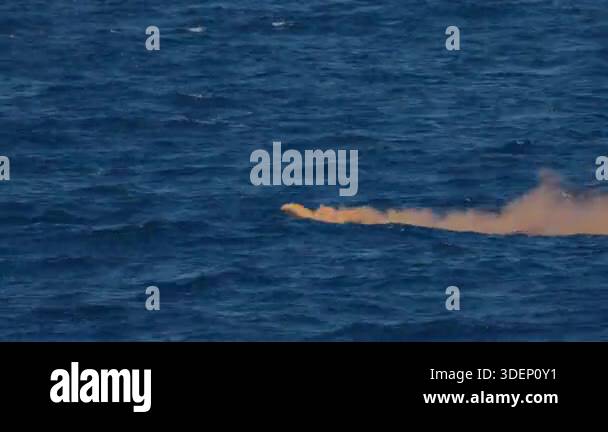 Orange smoke flare drifting on rough ocean water signaling emergency ...