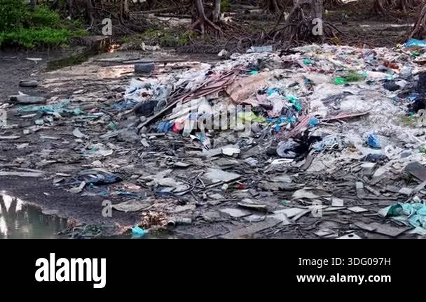 A pile of trash is on the ground next to a body of water. The trash ...