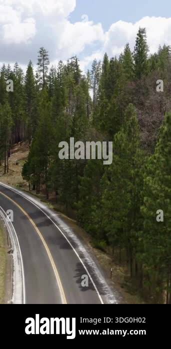 Aerial shot descends over a curving two-lane road cut through a dense ...