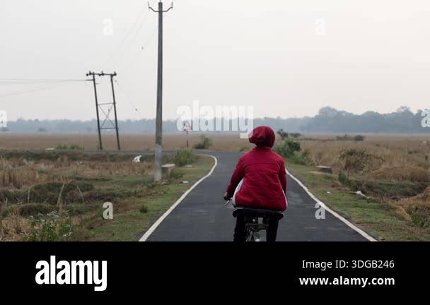 Assam, India January 2026:A person riding a bicycle along a narrow ...